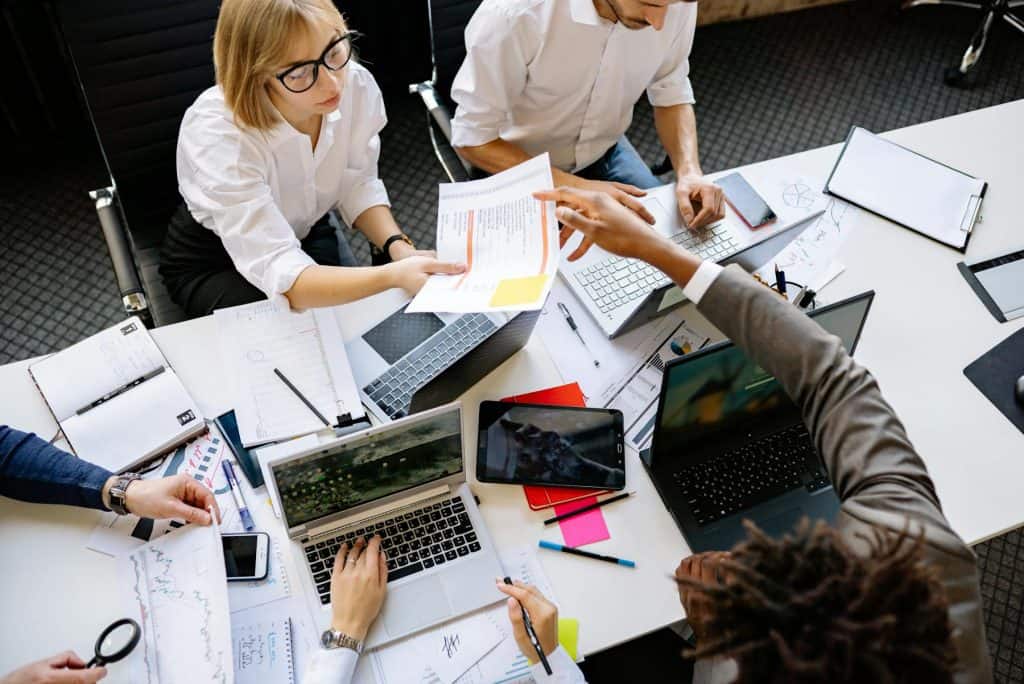 Team collaborating at a desk with laptops, documents, and charts during a work meeting