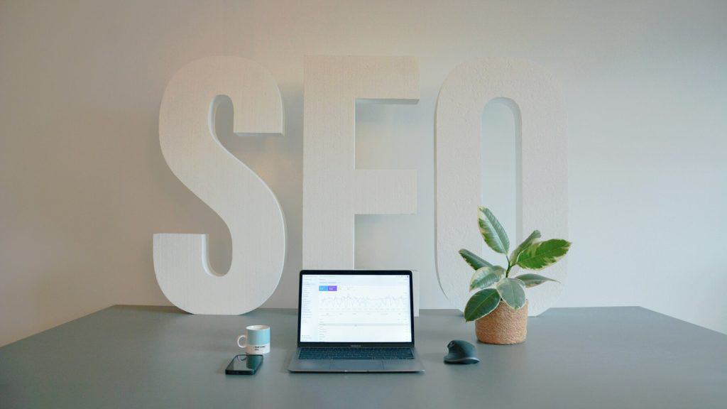 Minimal desk setup with laptop showing SEO analytics and large “SEO” letters in the background
