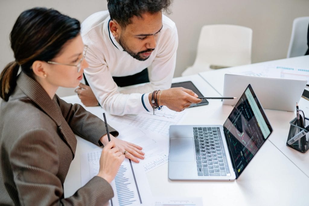 Two colleagues discussing a report in front of a laptop with documents on the table