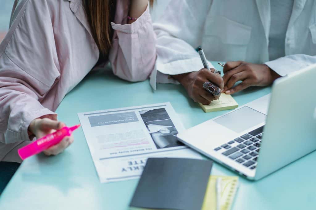Two colleagues working with an article in front of a laptop