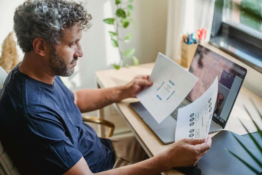 A man reading documents in front of his laptop