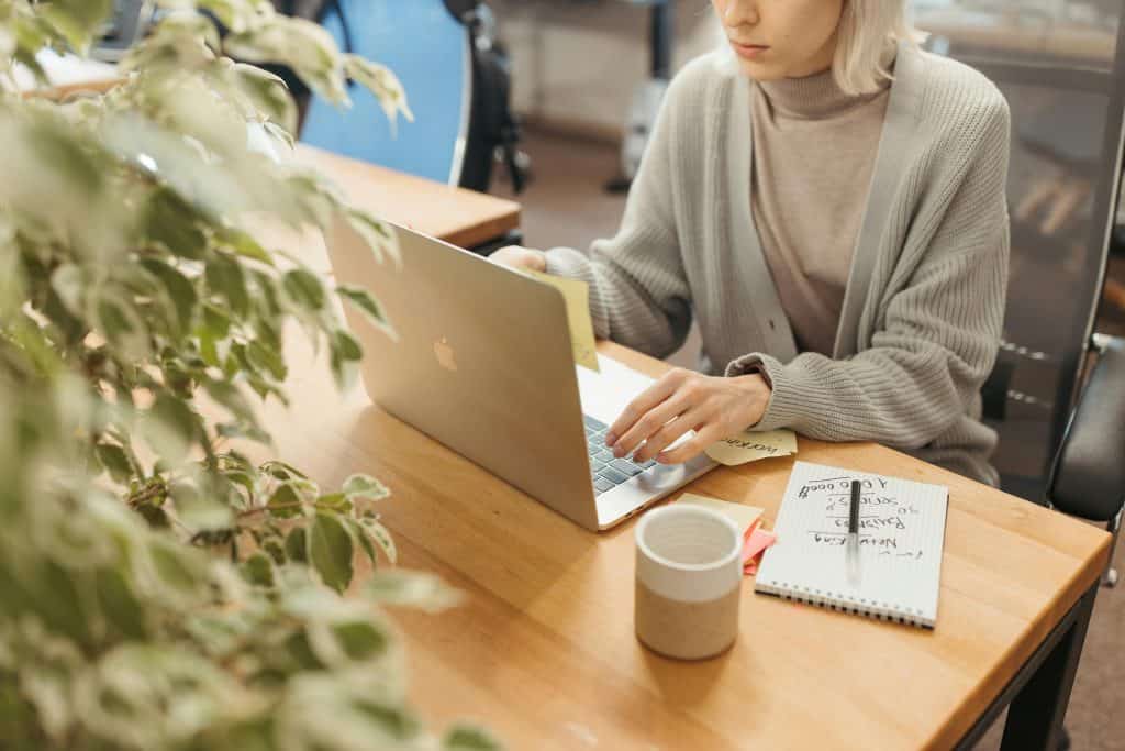 A woman typing in front of a silver laptop while holding a sticky note