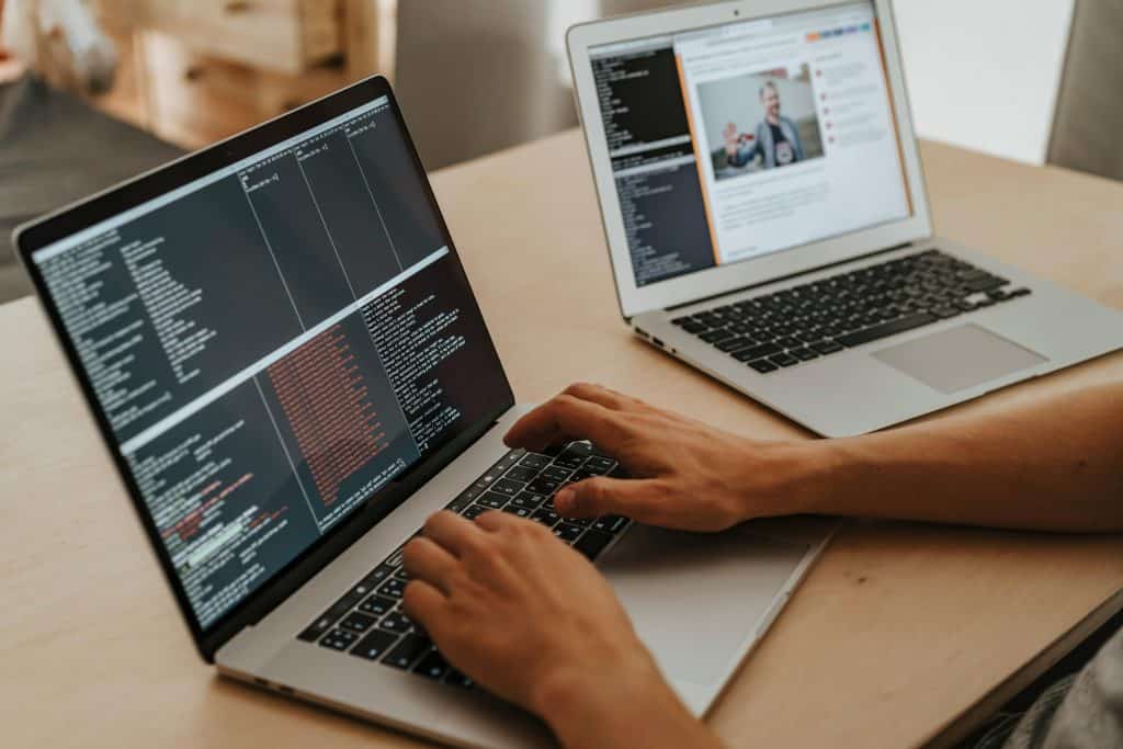 Hands of a person coding on two silver laptops