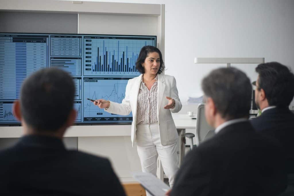 Businesswoman presenting data charts on large screens to a group