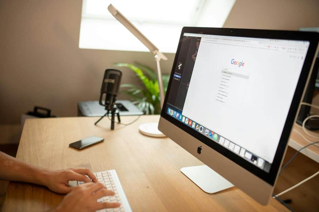 Person typing at an iMac showing a Google search page in a home office