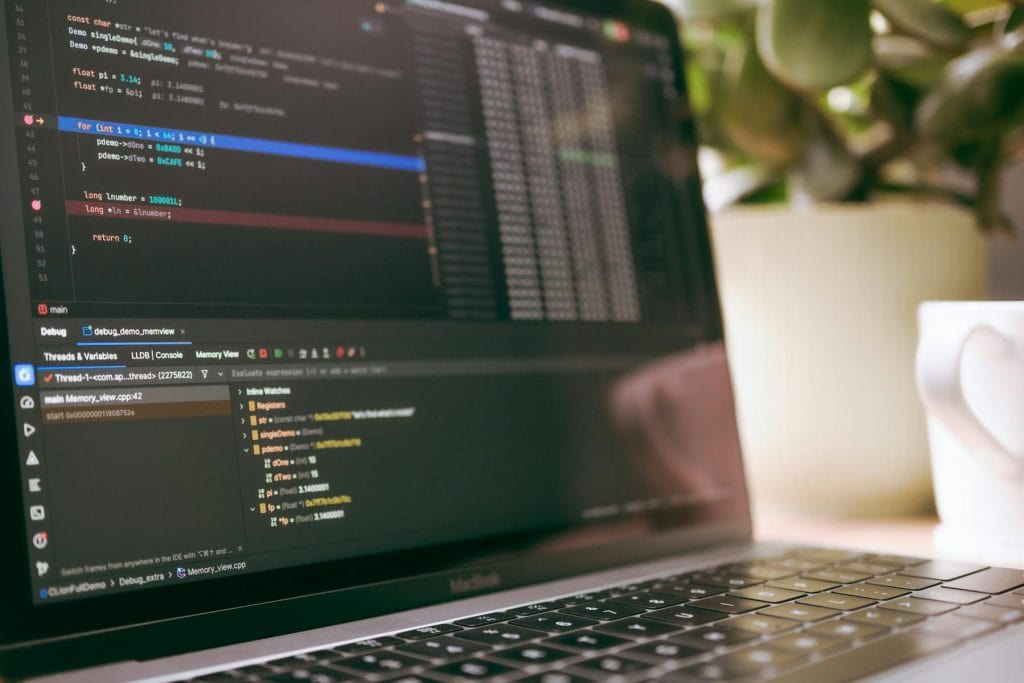 Close-up of a laptop screen displaying code and debugging tools beside a coffee mug and plant