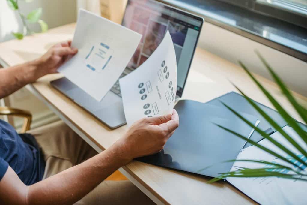 Person reviewing printed diagrams at a desk with an open laptop and folder