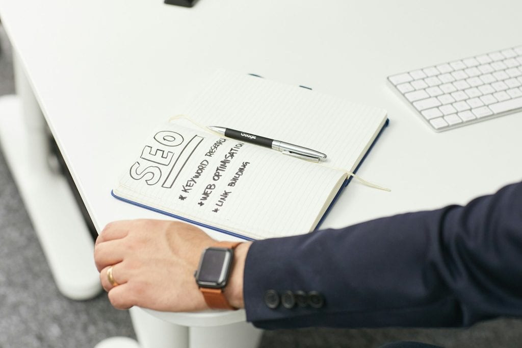 Person at a desk with an open notebook labeled SEO and notes on keyword research, web optimization, and link building