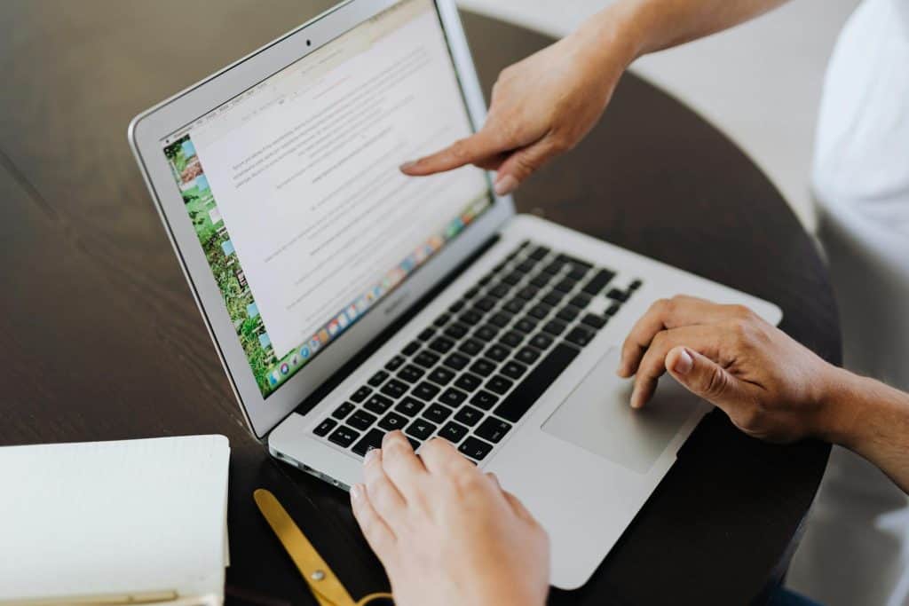 Two people working at a laptop, with one hand pointing at the screen