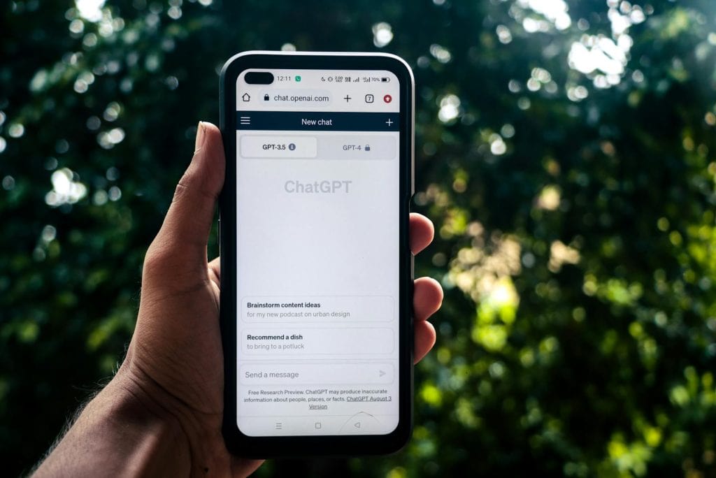 Hand holding a phone outdoors with the ChatGPT chat screen visible