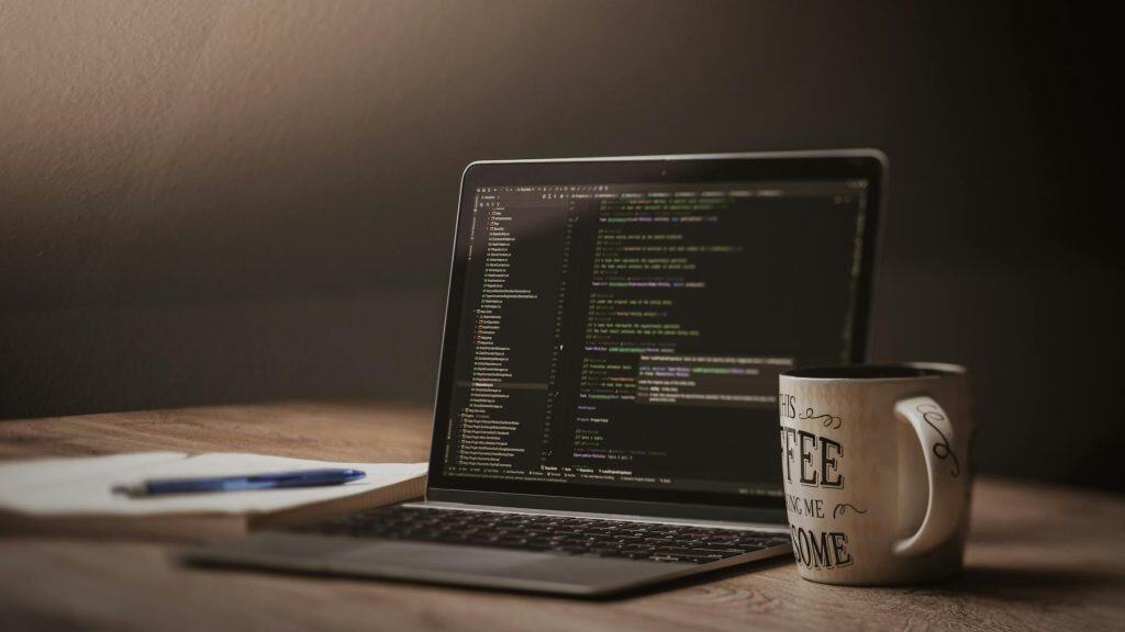 Laptop with code editor open beside a large coffee mug on a wooden desk