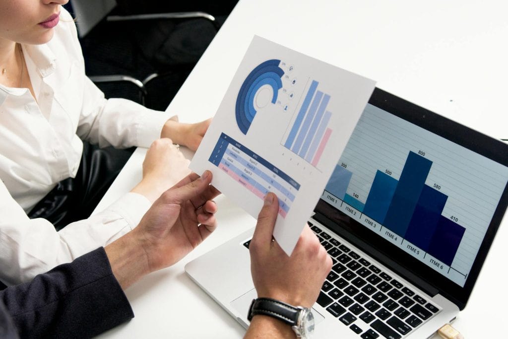 Colleagues reviewing printed charts beside a laptop with a bar graph