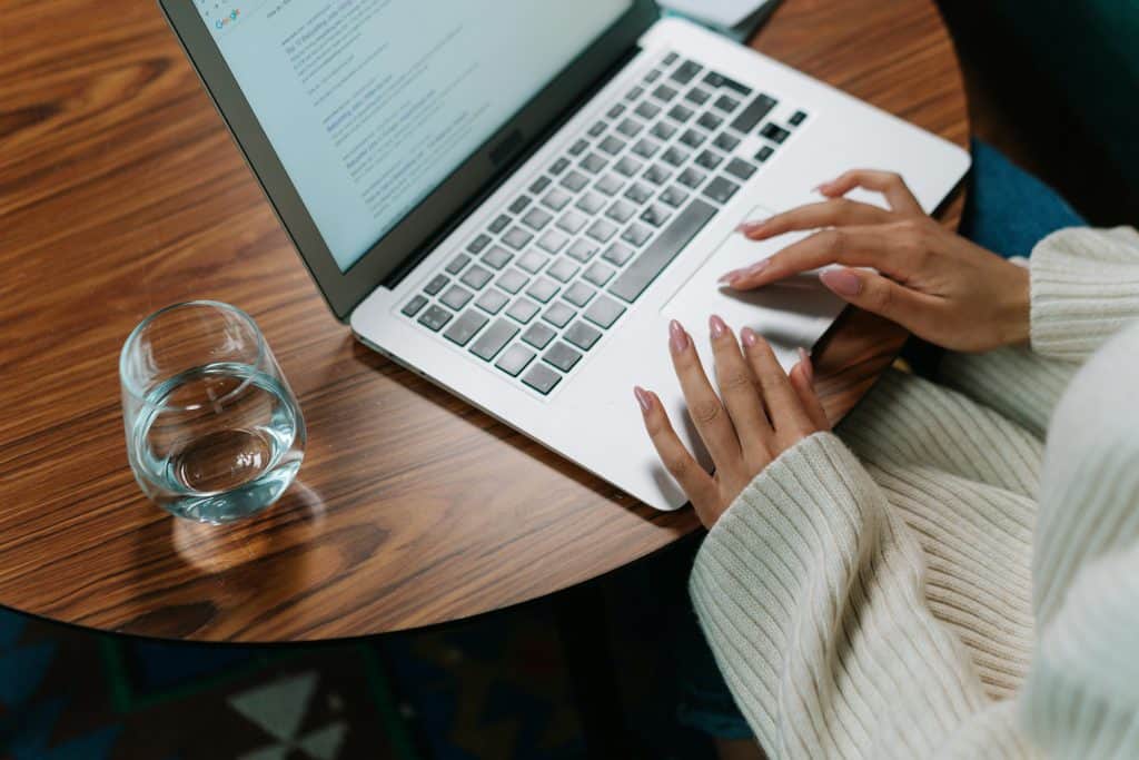 Hand of a woman typing on her laptop with a glass of water on the table