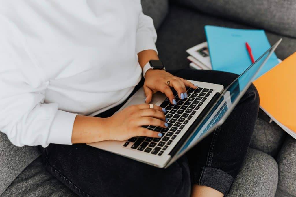 A woman sitting on a couch is typing on her laptop